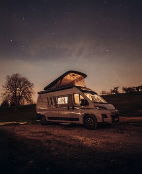 Carado Wohnmobil mit aufgeklapptem Aufstelldach nachts auf freiem Stellplatz unter Sternenhimmel