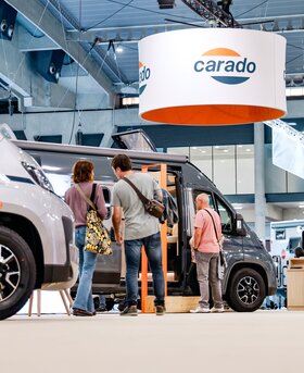 Visitors in front of a Carado motorhome at a trade fair, with the camper van open and the Carado logo above the stand