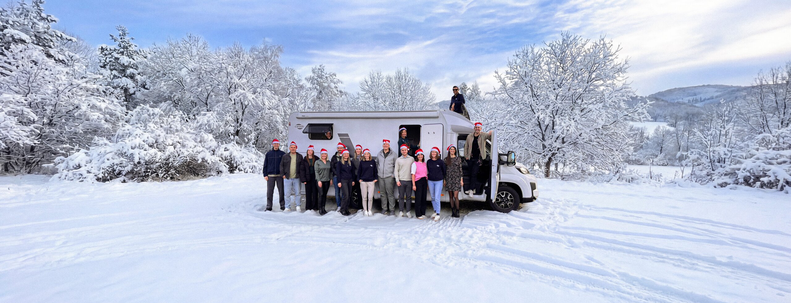 Gruppe mit Weihnachtsmützen vor Carado Wohnmobil auf verschneiter Winterlandschaft