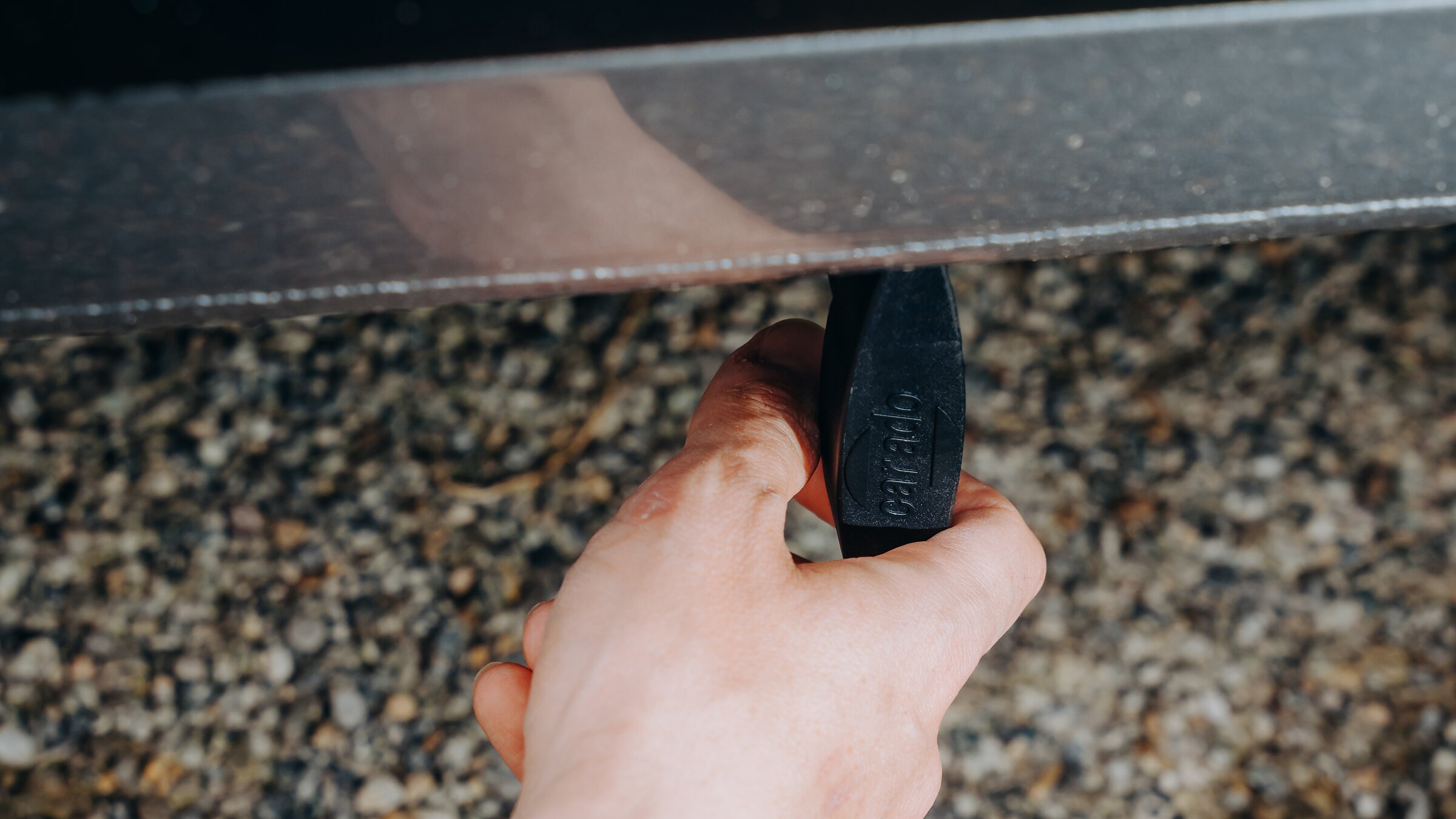 Nahaufnahme einer Hand, die einen schwarzen Hebel unter der Schürze eines Wohnmobils zum Ablassen des Abwassers greift und dreht.
