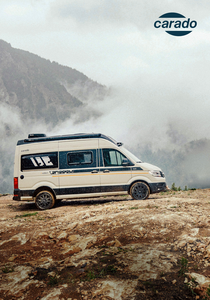 Carado motorhome with awning, table and two people on a meadow in front of a mountain backdrop