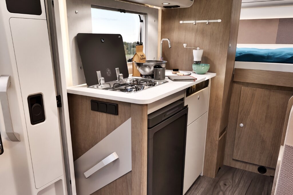 Innenraum Carado Wohnmobil mit Küchenzeile, Gasherd, Spüle, Kühlschrank und Bett im Hintergrund