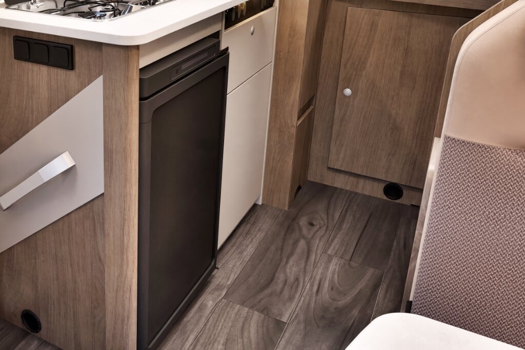 Küchenbereich im Carado Wohnmobil mit Gasherd, Spüle, Kühlschrank und Stauraum aus Holzdekor