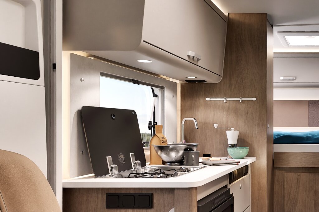 Innenraum Carado Wohnmobil mit Küche, Gasherd, Spüle, Oberschränken und Blick zum Bett im Heck