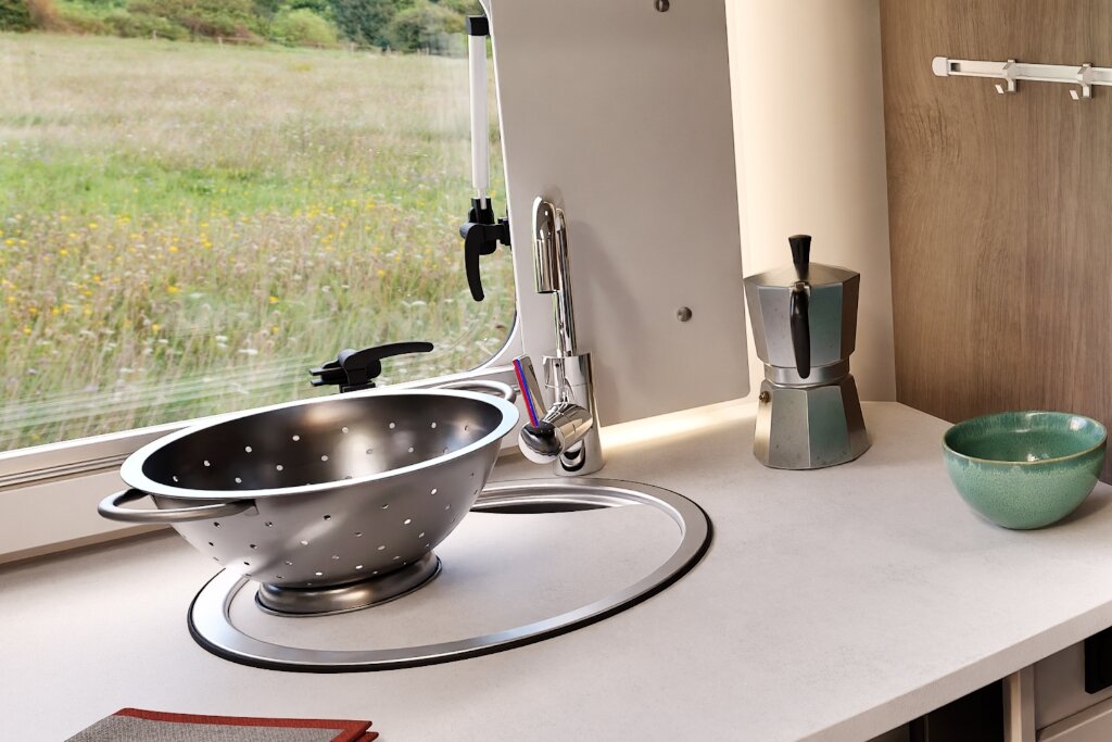 Küche im Carado Wohnmobil mit Spüle, Wasserhahn und Arbeitsfläche am Fenster