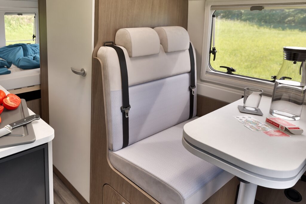 Sitzbank und Tisch im Innenraum eines Carado Wohnmobils, links Küche, hinten Bett und Fenster