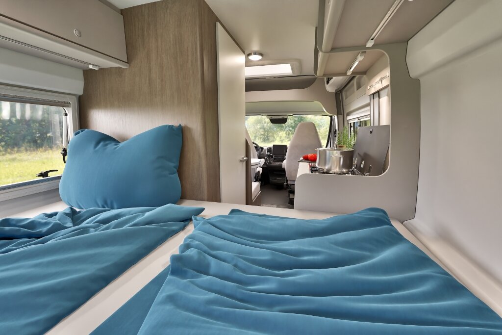 Schlafbereich im Carado Wohnmobil mit Doppelbett, blauer Bettwäsche und Blick zur Küche und Fahrerkabine