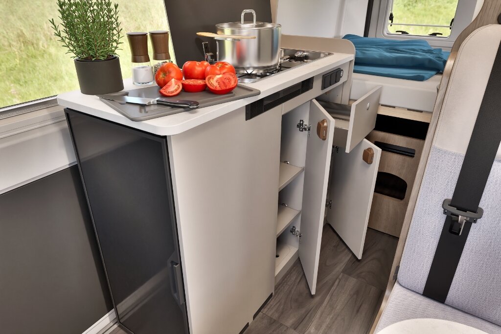 Innenraum Carado Wohnmobil mit Küche, Kochfeld, Spüle, geöffnete Schränke und Bett im Heck