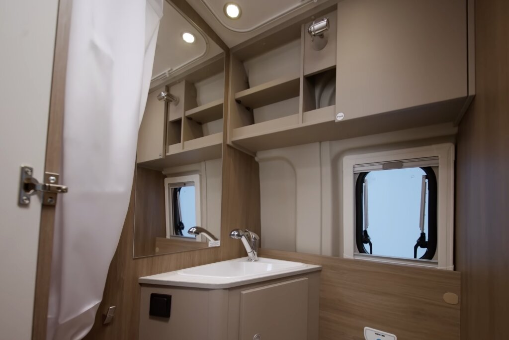 Badezimmer im Carado Wohnmobil mit Waschbecken, Spiegel, Hängeschränken und Fenster