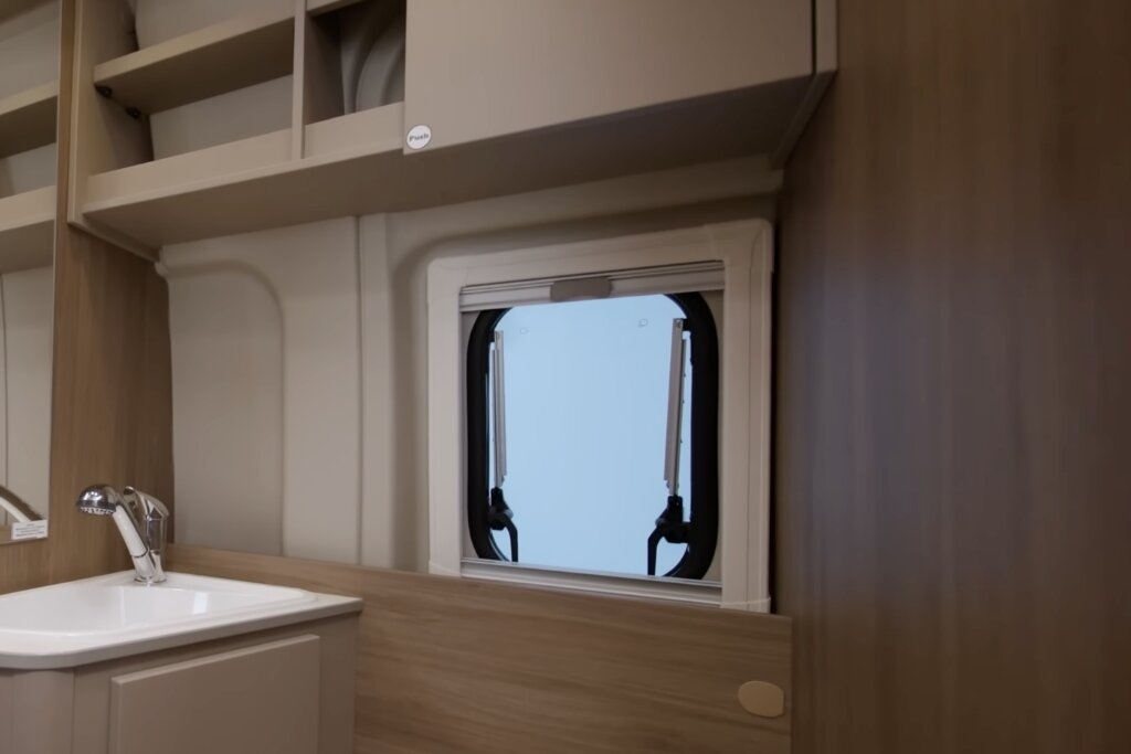 Waschbecken und Oberschränke im Innenraum eines Carado Wohnmobils mit Fenster und Holzverkleidung
