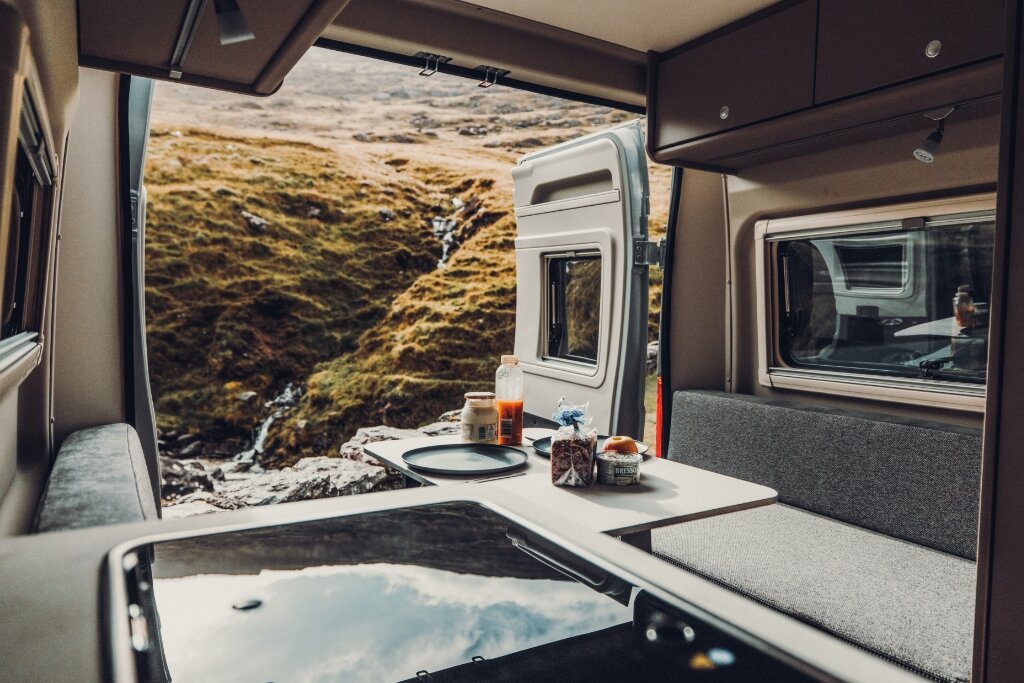 Innenraum Carado Wohnmobil mit Sitzbank, Tisch und offener Hecktür mit Blick auf felsige Landschaft