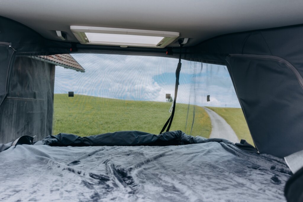 Blick aus dem Dachbett im Carado Wohnmobil auf Wiese und schmale Straße durch geöffnetes Frontfenster