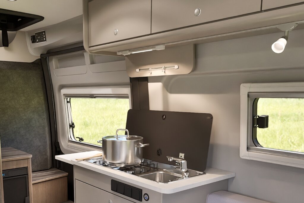 Küche im Carado Wohnmobil mit Gasherd, Spüle, Topf und Oberschränken neben zwei Fenstern