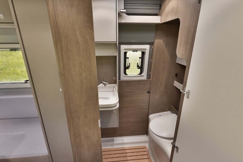 Bad im Carado Wohnmobil mit Waschbecken, Toilette, Fenster und Holzrost vor der Dusche