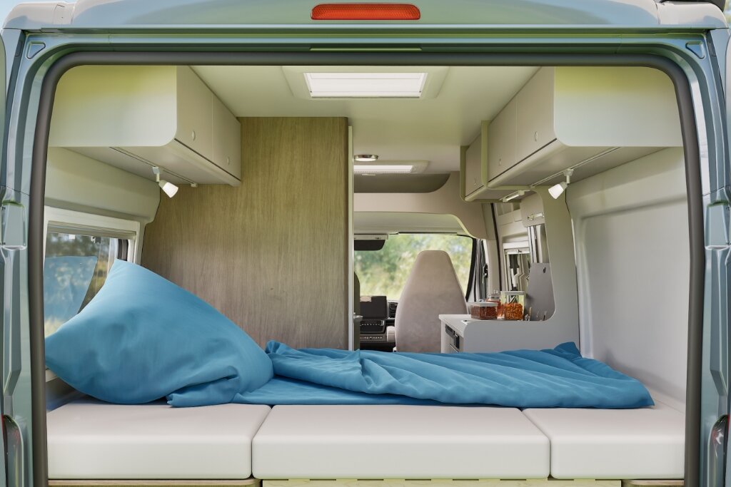 Heckbett im Carado Wohnmobil mit blauer Bettwäsche, Blick von hinten durch den Innenraum zur Küche