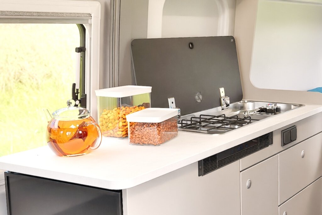 Küche im Carado Wohnmobil mit Gasherd, Spüle, Arbeitsfläche und Vorratsdosen am Fenster