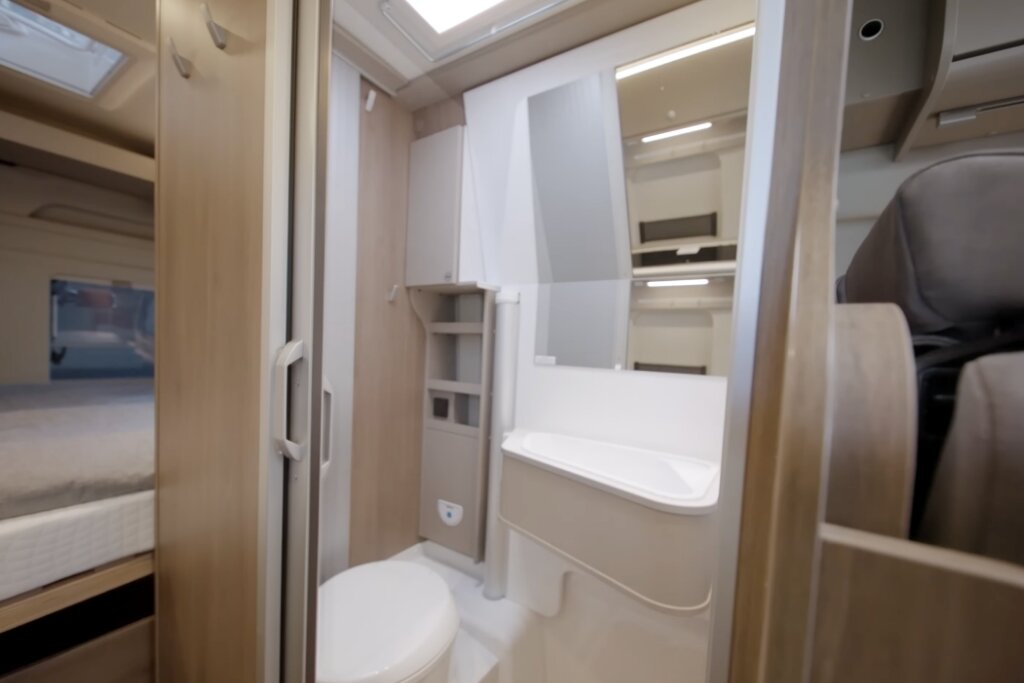 Bad im Carado Wohnmobil mit Waschbecken, Spiegel, Toilette und Blick zum Schlafbereich