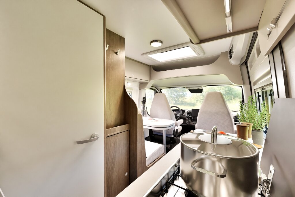 Innenraum Carado Wohnmobil mit Küche, Topf auf Gasherd und Sitzgruppe im Fahrerhaus