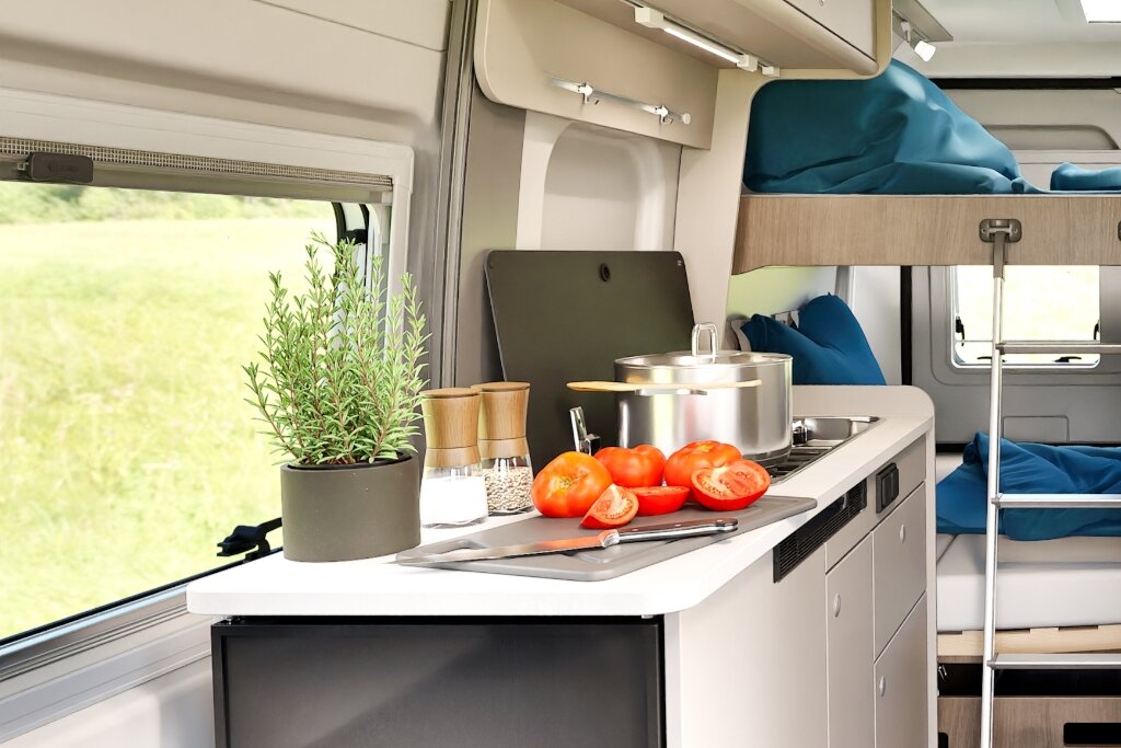 Innenraum Carado Wohnmobil mit Küche, Tomaten auf Arbeitsfläche und Etagenbetten im Hintergrund