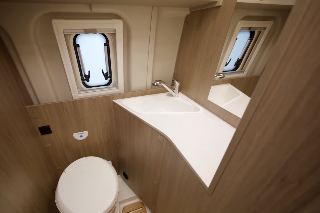 Badezimmer im Carado Wohnmobil mit Waschbecken, Spiegel, Toilette und zwei Fenstern