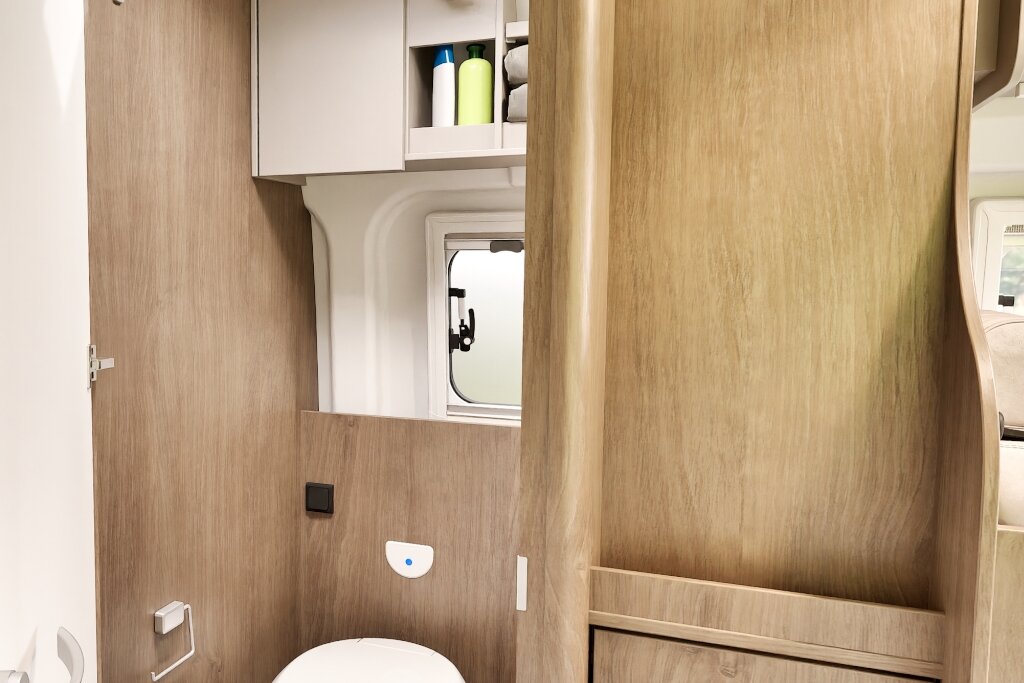 Bad im Carado Wohnmobil mit Toilette, Spiegel, Fenster und offenem Hängeschrank