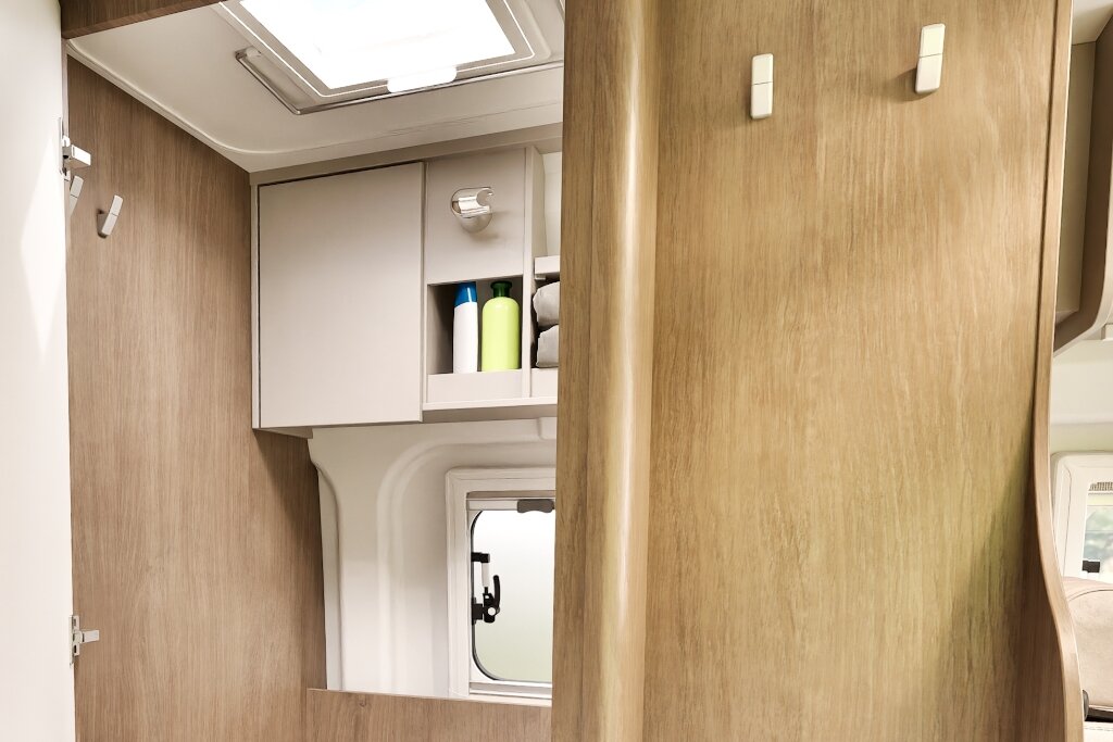 Bad im Carado Wohnmobil mit Hängeschrank, offenem Regal, Dachfenster und kleinem Seitenfenster