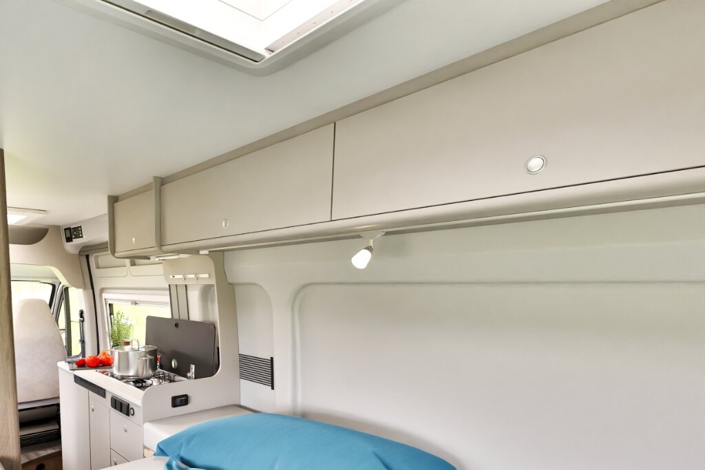Innenraum Carado Wohnmobil mit Küche, Hängeschränken, Dachfenster und Bett im Vordergrund