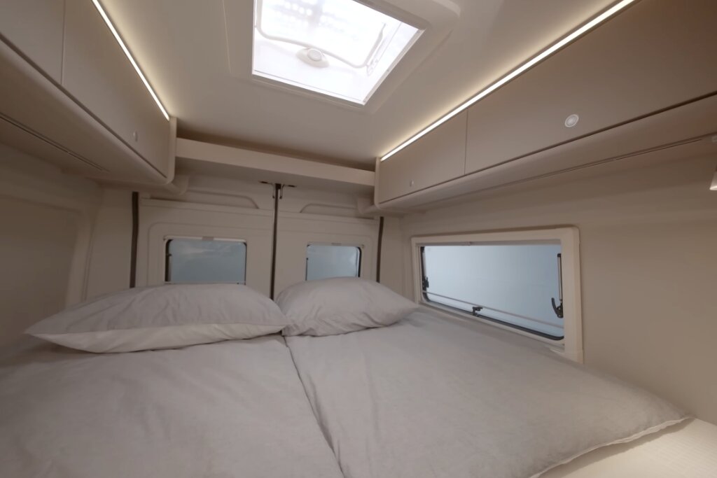 Schlafbereich im Carado Wohnmobil mit Doppelbett, Dachfenster, seitlichen Hängeschränken und Fenstern