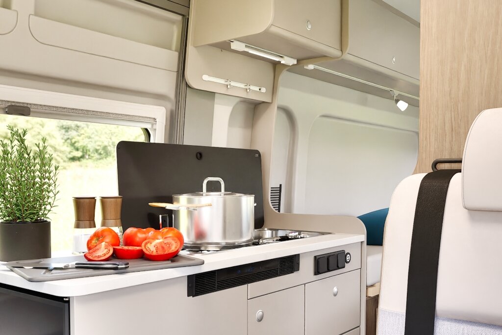 Küche im Carado Wohnmobil mit Kochtopf, geschnittenen Tomaten, Spüle und Stauraum
