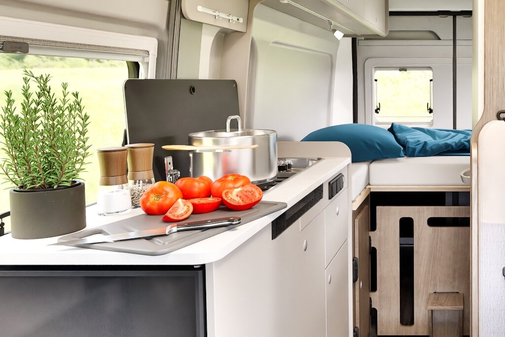 Innenraum Carado Wohnmobil mit Küche, Tomaten auf Schneidebrett und Bett im Heck