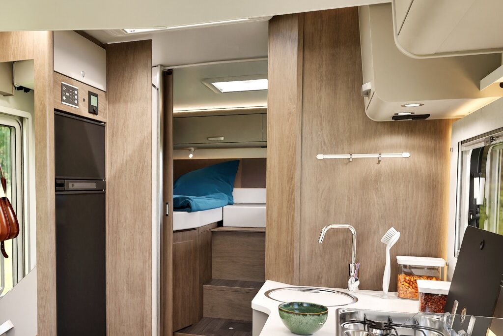 Innenraum Carado Wohnmobil mit Küche, Kühlschrank und erhöhtem Bett im Heck