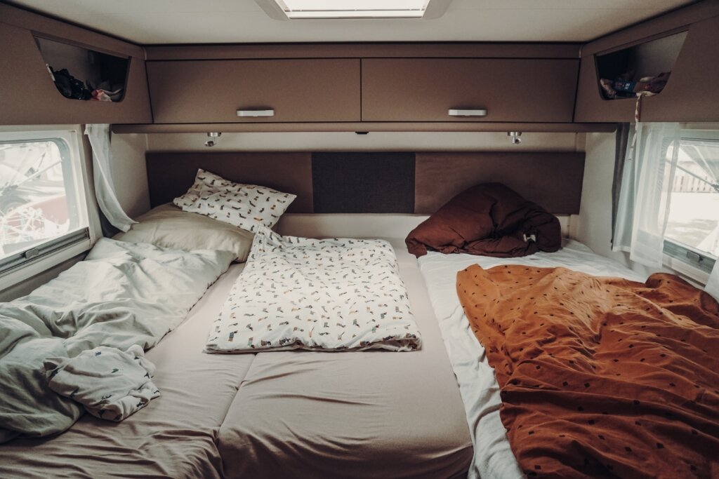 Schlafbereich im Carado Wohnmobil mit Doppelbett, Kissen, Decken, Dachfenster und Hängeschränken