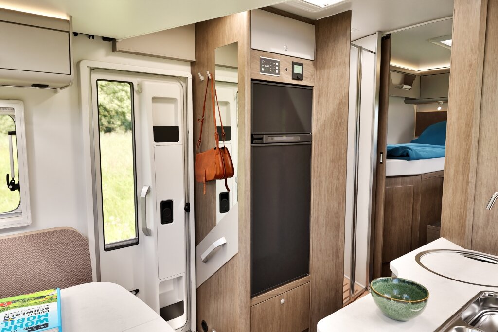 Innenraum Carado Wohnmobil mit Eingang, Kühlschrank, Küche und Blick zum Bett im Heck