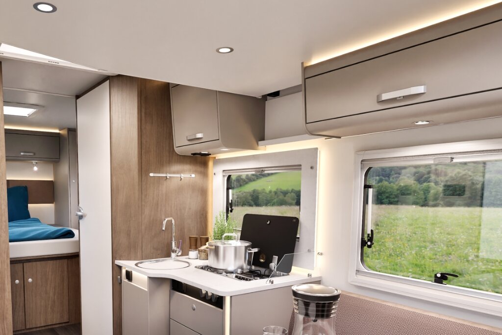 Carado motorhome interior with kitchen, gas hob, sink, overhead cabinets and a view towards the rear bed