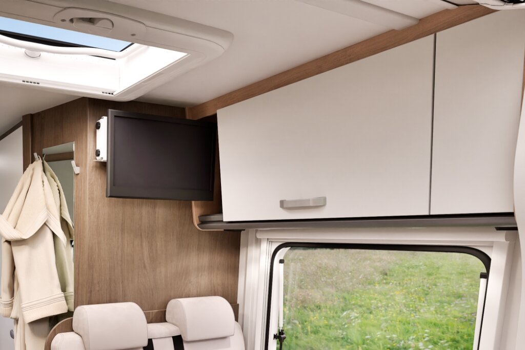 Innenraum Carado Wohnmobil mit Hängeschrank, TV, Dachfenster und Fenster über den Sitzen