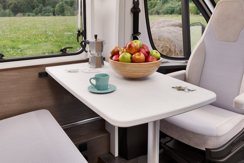 Sitzgruppe im Carado Wohnmobil mit Tisch, Obstschale, Tasse und Kaffeekanne am Fenster