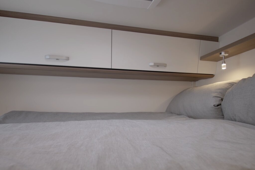 Schlafbereich im Carado Wohnmobil mit Doppelbett, Oberschränken und Leselampe