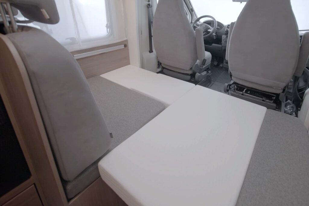 Carado Wohnmobil Innenraum mit umgebauter Sitzgruppe als Bett im Fahrerhausbereich