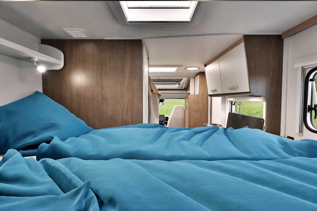Schlafbereich im Carado Wohnmobil mit blau bezogenem Bett und Blick in den Innenraum