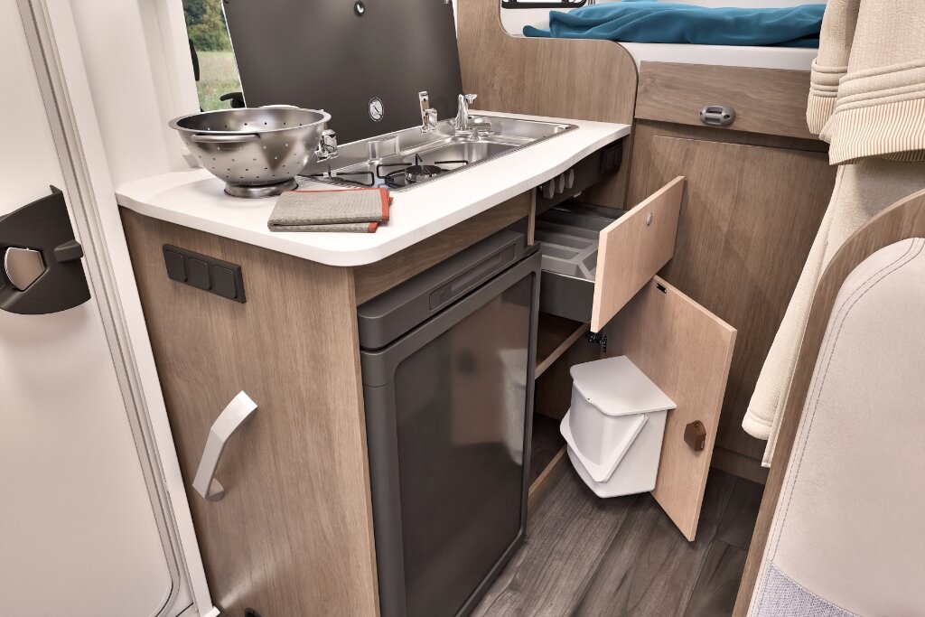 Küche im Carado Wohnmobil mit Spüle, Gaskocher, Kühlschrank und geöffnetem Stauraum