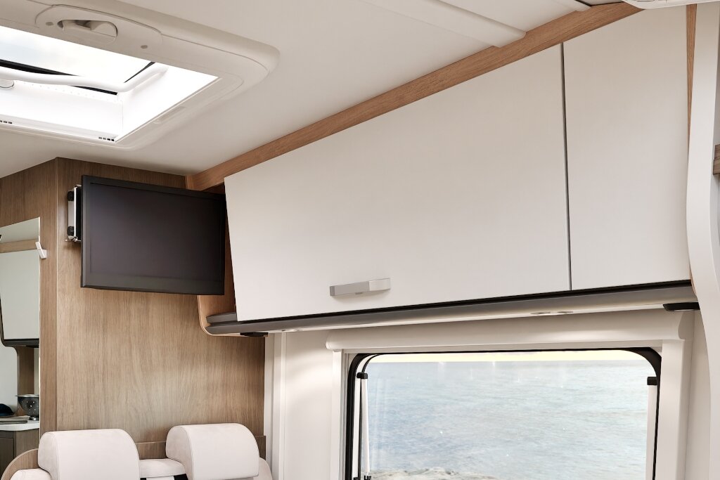 Innenraum Carado Wohnmobil mit Hängeschrank, Dachfenster und TV über Sitzplätzen
