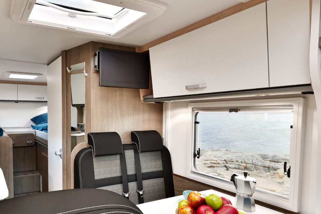 Innenraum Carado Wohnmobil mit Sitzbank, Oberschränken, Dachfenster, TV und Fensterblick aufs Wasser