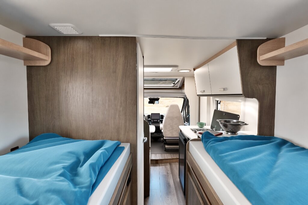 Innenraum Carado Wohnmobil mit zwei Einzelbetten, Küchenzeile und Blick nach vorn ins Fahrerhaus
