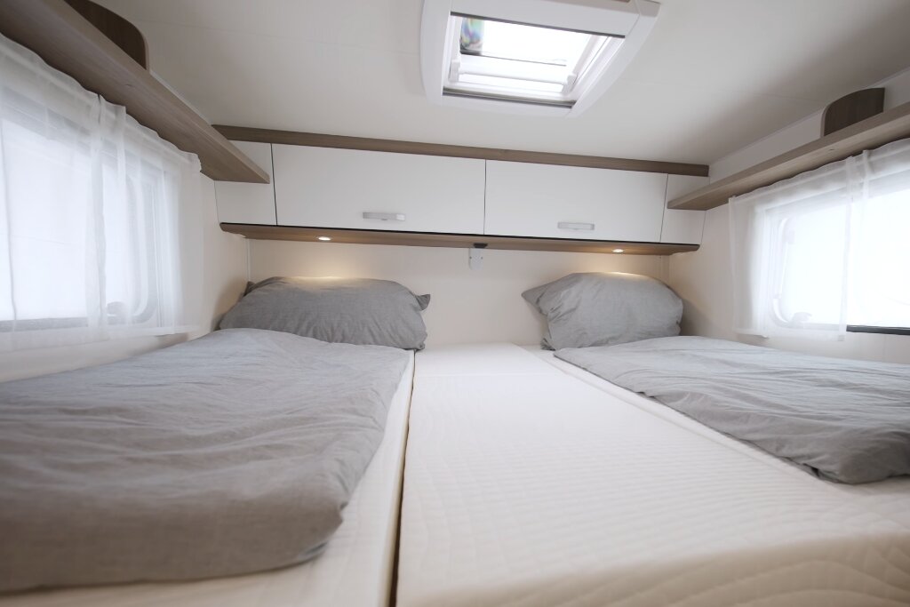 Schlafbereich im Carado Wohnmobil mit zwei Einzelbetten, Dachfenster und Oberschränken