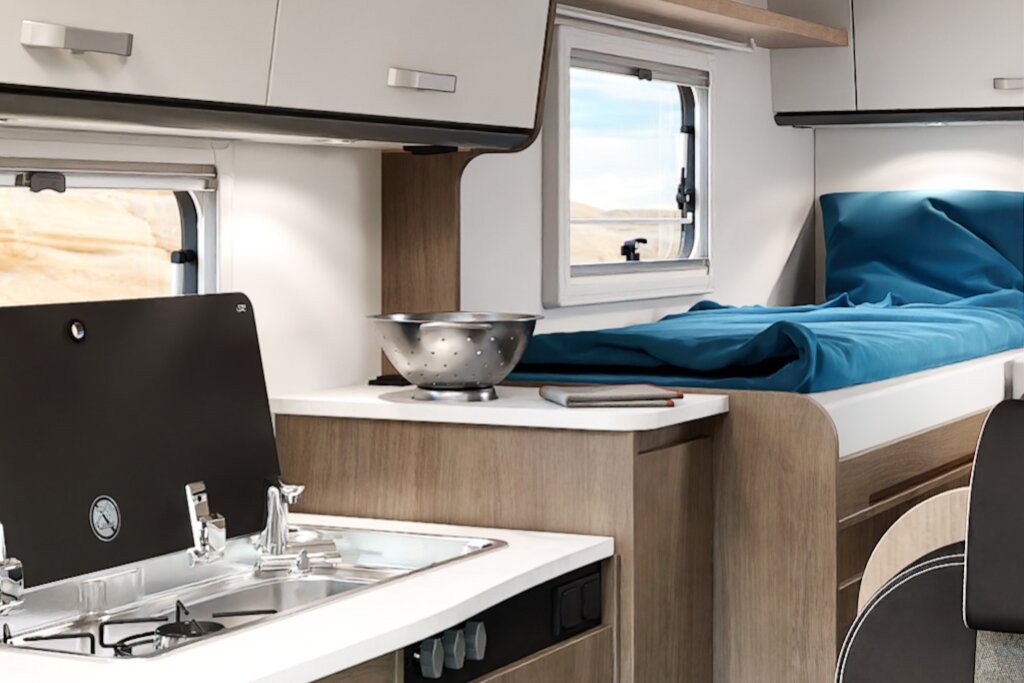 Innenraum Carado Wohnmobil mit Küche, Spüle, Gasherd und Einzelbett neben Fenstern
