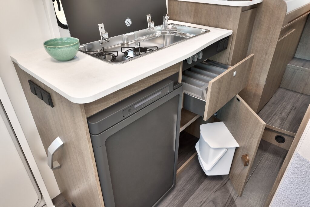 Küche im Carado Wohnmobil mit Spüle, Gasherd, Kühlschrank und geöffneten Schubladen