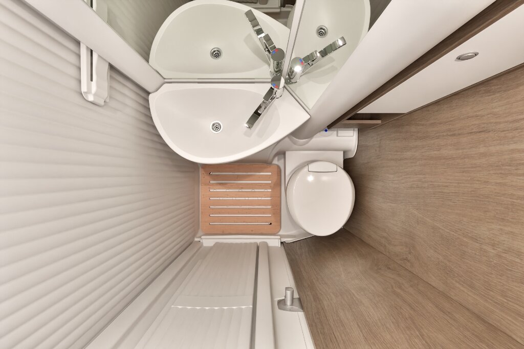Bad im Carado Wohnmobil mit Eckwaschbecken, Toilette, Holzrost und Rollowand