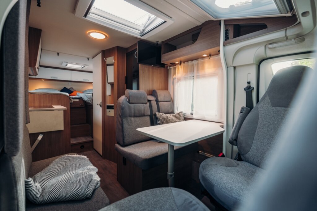 Innenraum Carado Wohnmobil mit Sitzgruppe, Tisch, Dachfenster und Bett im Heck