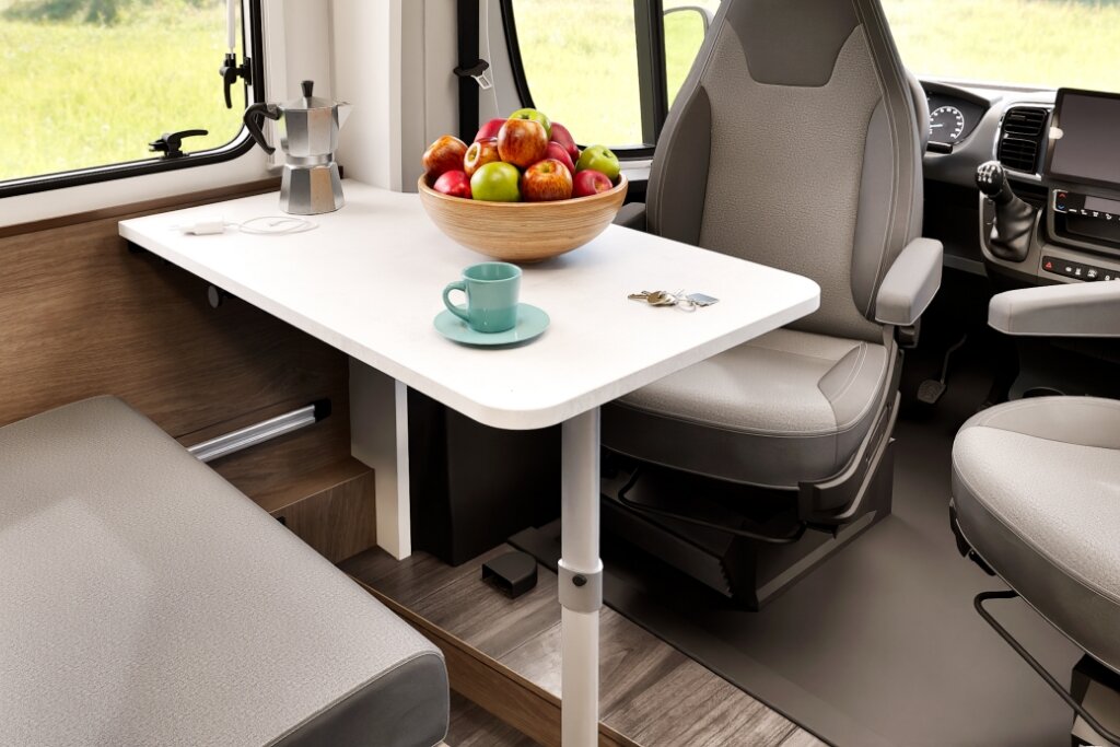 Sitzgruppe im Carado Wohnmobil mit Tisch, gedrehten Fahrersitzen, Obstschale und Tasse