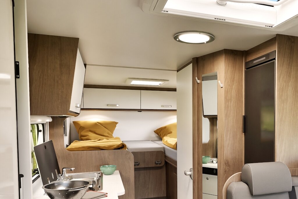 Innenraum Carado Wohnmobil mit Einzelbetten, Küchenzeile, Kühlschrank und Stauraum in Holzoptik